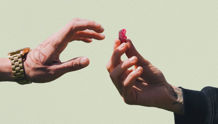 Deux mains tendues l'une vers l'autre, l'une tatouée, tenant un bonbon rouge au THC.