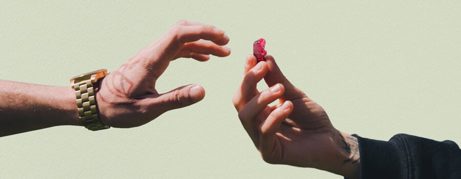 Deux mains tendues l'une vers l'autre, l'une tatouée, tenant un bonbon rouge au THC.