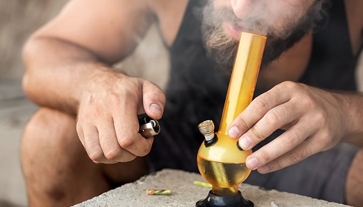 Personne fumant du haschich d'un bong en verre, expirant de la fumée épaisse.